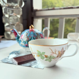 swirling leaves teacup on table with chocolate and teapot